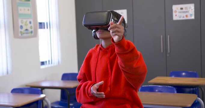 Male youth in red hoodie putting on black VR headset in classroom, pointing, navigating VR