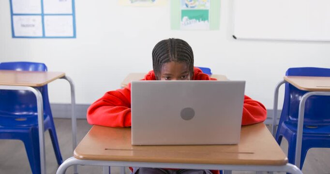 African American teen working on laptop at class desk completing assignment as camera pulling back