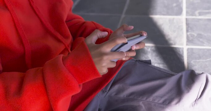 Teen male in red hoodie gripping foldable phone, adjusting and swiping on tiled walkway, copy space
