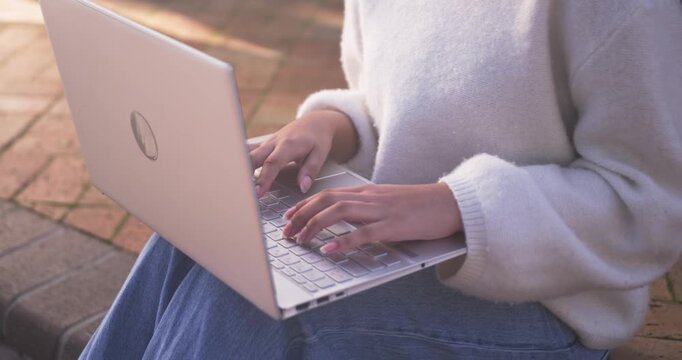 Child female lifting hands, typing steadily on silver laptop on patio in fuzzy sweater doing work