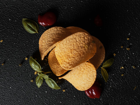 Top view of a stack of chips with basil and ketchup on black background