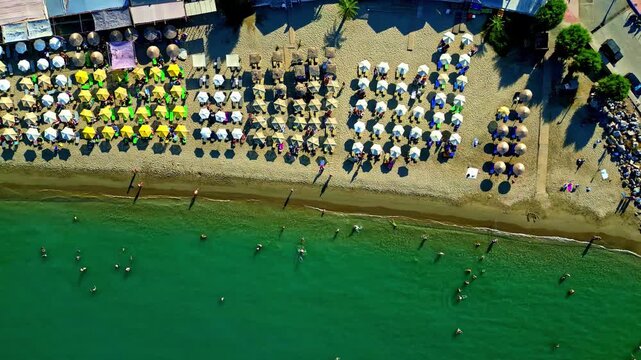 Aerial view of Crete beach with rows of colorful umbrellas on the sand and people swimming in the clear turquoise water of the Mediterranean Sea, Greece.