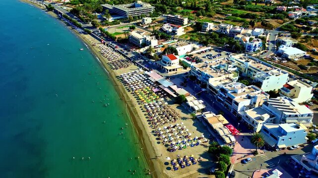 Aerial view of the sandy beach in Crete with rows of colorful umbrellas along the turquoise coastline in Greece.