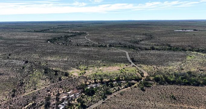 Panoramic drone view of the vast Great Karoo near Prince Albert in the Western Cape, South Africa. A winding gravel road crosses a seasonal river bordered by indigenous vegetation.