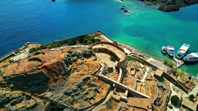 Aerial view of the historic Spinalonga fortress ruins surrounded by turquoise waters and boats in Crete, Greece.