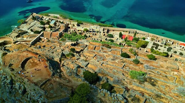 Aerial view of the historic stone ruins and fortifications of Spinalonga island surrounded by clear turquoise waters in Crete, Greece.