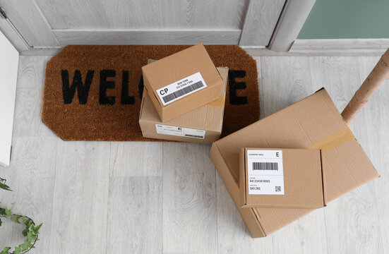 Cardboard delivery boxes on a welcome mat at a residential doorstep, online shopping and shipping concept, the packages feature shipping labels with barcodes and tracking information