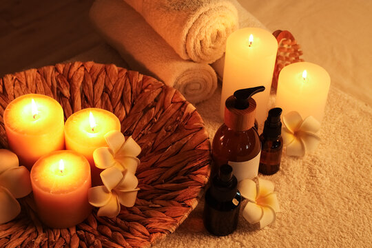 Spa treatment setup with burning candles, essential oils, and rolled towels for relaxation and wellness