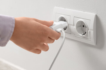 Naklejka premium Person plugging white charger into a wall power outlet, electricity and energy supply concept, close up