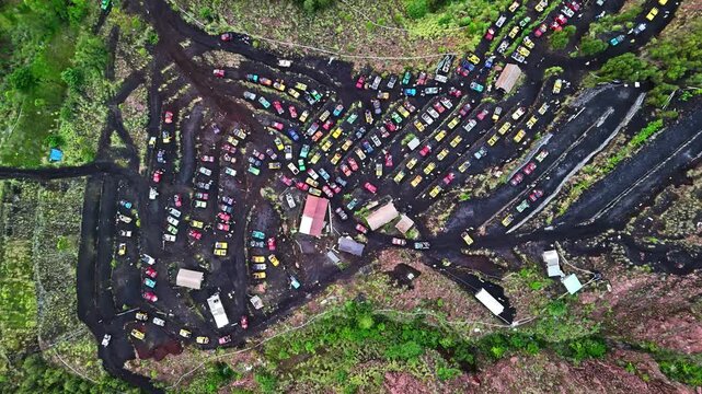 Aerial view of numerous colorful off-road jeeps parked in rows on dark volcanic terrain surrounded by lush green vegetation in Bali, Indonesia.