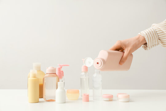 Woman pouring cosmetic product into travel bottle on light background