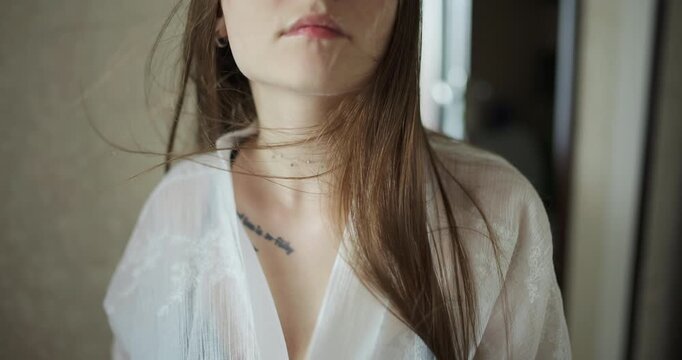 Soft relaxed pretty woman in peignoir looking aside while hair blowing in slow motion