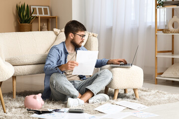 Fototapeta premium Young man in debt with paper using laptop at home