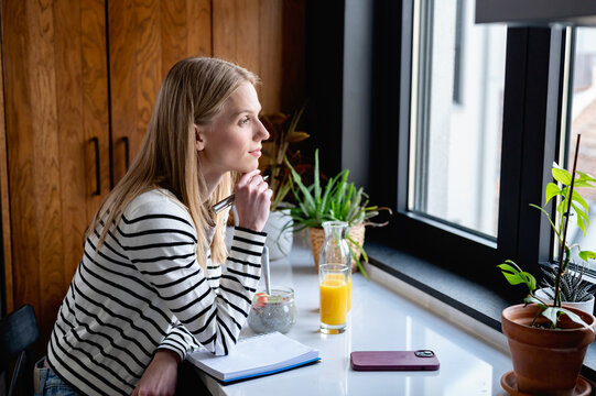 Thoughtful woman journaling beside a nutritious breakfast in a sunlit kitchen, representing mindfulness, healthy habits, personal growth and intentional daily routines