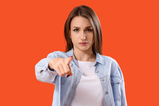 Young woman pointing at viewer on orange background, closeup. Accusation concept