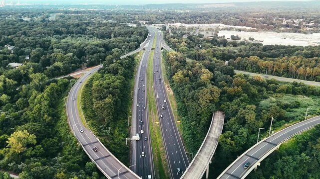 Aerial view of Connecticut highway interchange with traffic through green forest, representing transportation infrastructure, commuting, mobility, and regional connectivity. 4K.