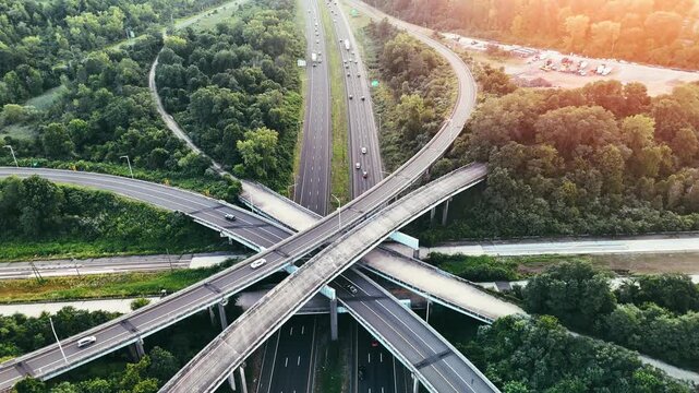 Scenic aerial view of a modern highway interchange crossing a green forest with steady traffic during sunset, symbolizing transportation networks and urban connectivity.