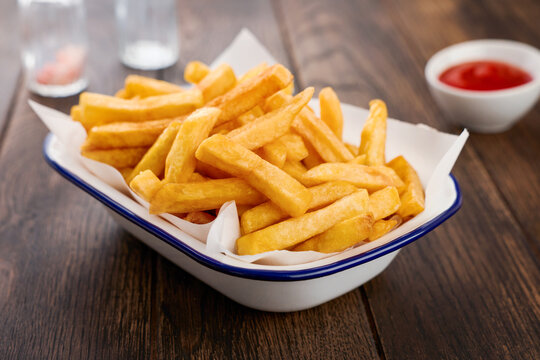 Close-up of golden french fries in enamel tray with ketchup on wooden table, fast food snack concept for cafe menu, restaurant advertising, takeaway food, street food, lunch, appetizer, delivery promo