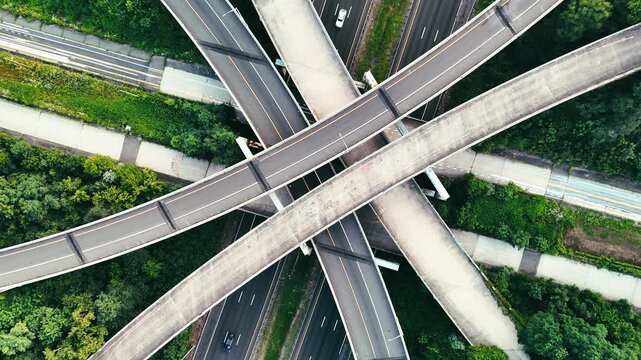 Aerial view of vehicles moving through layered highway overpasses in an urban green corridor, symbolizing rush hour, commuting, infrastructure, mobility, and city transport. 4K.