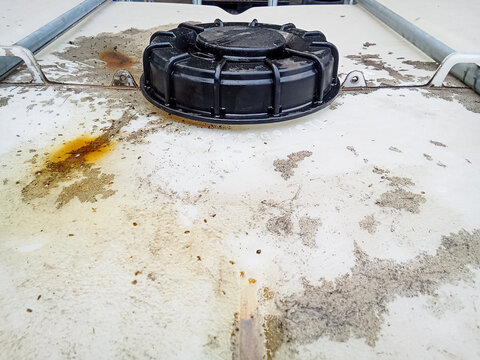 Close up view of black plastic cap on dirty white industrial IBC tote tank reservoir container with metal frame