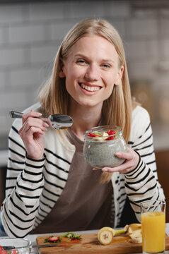 Close-up of a woman enjoying creamy chia pudding topped with strawberries and banana in a modern kitchen, ideal for concepts of healthy living, nutrition and home cooking