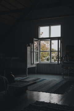 Laane County, Estonia - 02 June 2024: View of a rustic room with an open window looking out onto lush foliage, featuring a wooden bed frame, a patterned rug, and soft natural light.