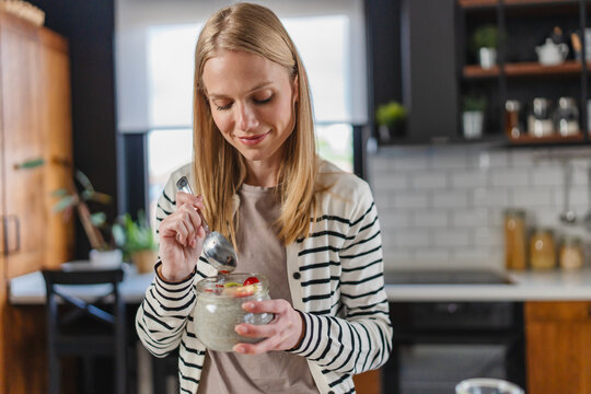 Young woman enjoying a healthy breakfast with overnight oats and fresh fruit in a modern kitchen. Balanced nutrition, morning routine, healthy lifestyle, wellness and home comfort concept
