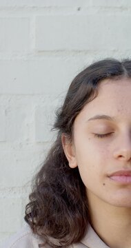 Vertical video: African American teen opening eyes by sun, smiling by white brick wall, copy space