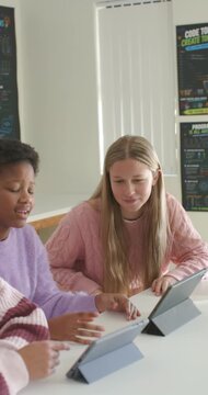 Vertical video: Diverse teen girls in class, peer tapping tablets, blonde in pink sweater learning