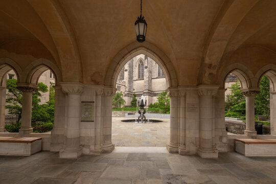 Washington, District of Columbia, United States - 06 May 2025: View of Washington National Cathedral, featuring a stone cloister with arched walkways, a central fountain, and lush greenery.