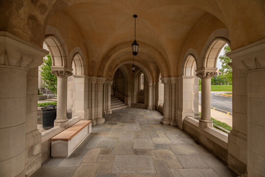 Washington, United States - 06 May 2025: View of Washington National Cathedral featuring a stone arched walkway with vaulted ceilings, hanging lanterns, and a wooden bench.