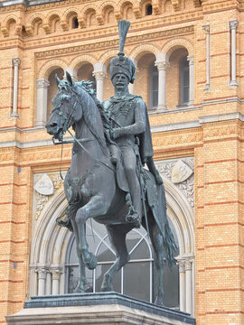 Hanover, Germany - 29 March 2026: View of the Ernst August monument, a bronze equestrian statue of King Ernst August I, set against the ornate yellow brick facade of the station.