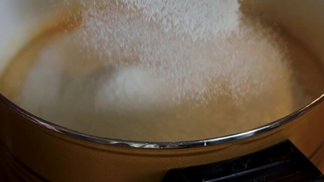 Flour being sifted through a metal sieve into smooth batter in a saucepan.