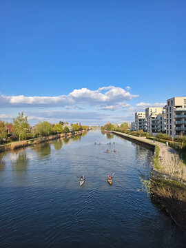 Hannover, Germany - 14 April 2026: View of kayakers paddling on the calm waters of the canal near Holzwiesen, with modern apartment buildings along the bank under a clear blue sky.