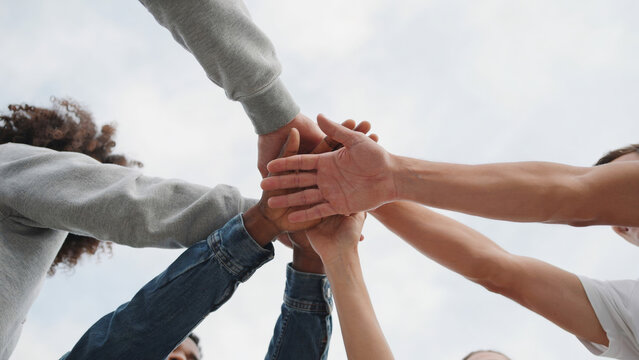 Diverse group of friends stacking hands together in unity and support, celebrating teamwork.