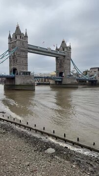 Tower Bridge spans the River Thames under dramatic overcast skies in London, England, showcasing one of the city's most iconic Victorian bascule bridges