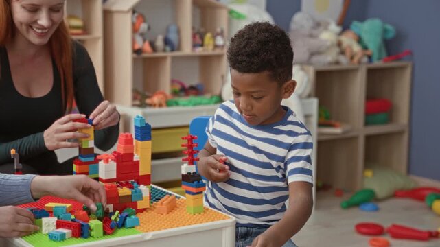 Woman and boy stacking colorful plastic blocks at a preschool classroom table inside a building; playful learning.