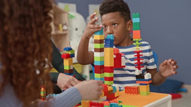 Boy stacking colorful toy blocks with hand placing a brick on a tall plastic tower in a playroom building; concentration.