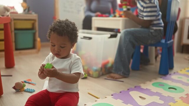 Toddler boy sits on foam number mat holding and examining toy blocks with focused hands in a building playroom; nurturing calm.