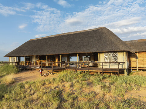 Kgalagadi South, Kgalagadi District, Botswana - 06 February 2026: View of Rooiputs Lodge with a thatched roof and wooden deck in the desert landscape.