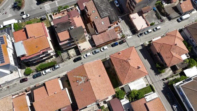 Top down aerial drone view of residential houses with orange tile roofs and streets with parked cars during sunny day in town in Italy.