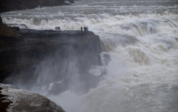 Tourists standing on a cliff at gullfoss, experiencing the immense power of the golden waterfall and glacial river hvita. Iceland golden tourism route