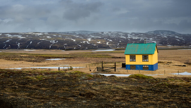 Charming isolated yellow house with a green roof in a desolate Icelandic tundra landscape under dark stormy skies.
