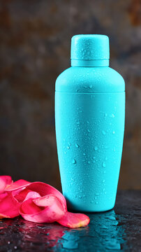 Blue cocktail shaker with water droplets and pink petals on reflective surface