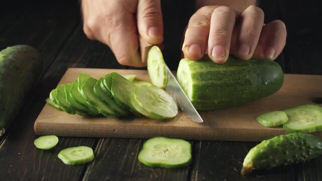 Hands slicing fresh cucumber into thin rounds on a wooden cutting board, with additional cucumber pieces and a knife visible, creating a vibrant kitchen scene with natural lighting