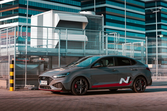 A Hyundai i30 N is parked beside tall buildings under clear skies in a city environment  Katowice, Poland, 19.06.2021
