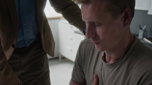 Young adult Caucasian male veteran wearing dog tags receiving support from unknown therapist during counseling session. Ideal for mental health awareness and PTSD therapy advertisements