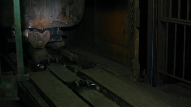 Close-up of a rusty minecart being pushed into an elevator cage on rails in a dark underground mine. Industrial automation and heavy machinery concept.