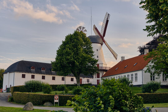 Sonderborg, Denmark - 07 July 2026: View of Dybol Mill during sunset hours with white walls, red roof tiles, and lush green trees under a soft evening sky.