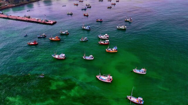 Aerial view of numerous small fishing boats anchored in the clear turquoise waters of a bay with a pier visible in the background in Sri Lanka.